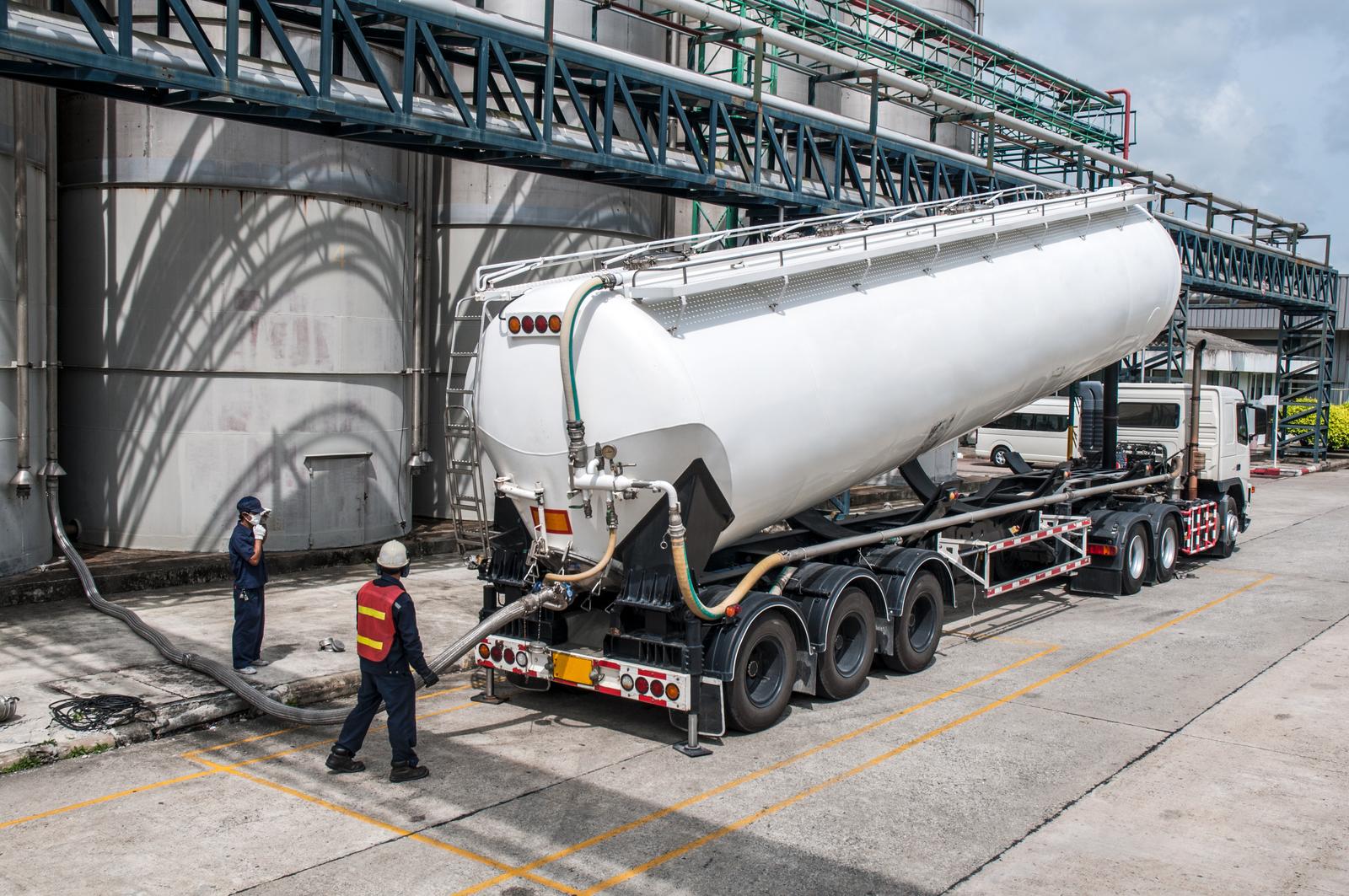 Bulk powder tanker being loaded under a silo with workers in safety gear