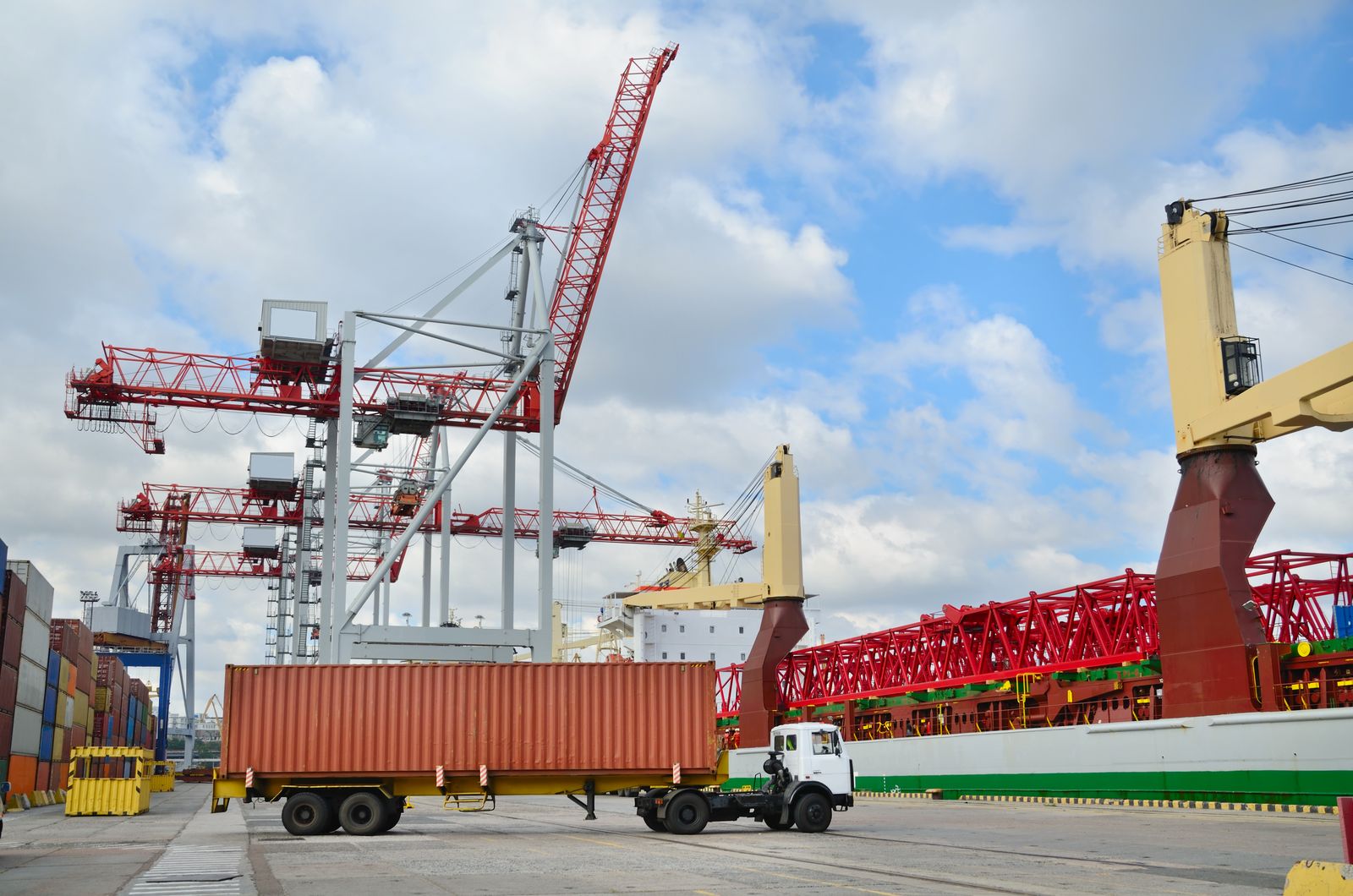 Container truck beside quay cranes at a port terminal
