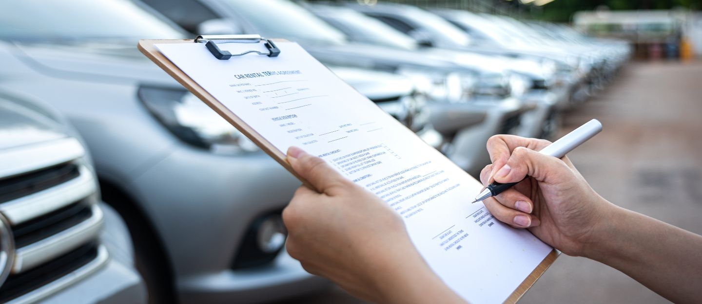 Person filling in a checklist on a clipboard beside a row of parked cars