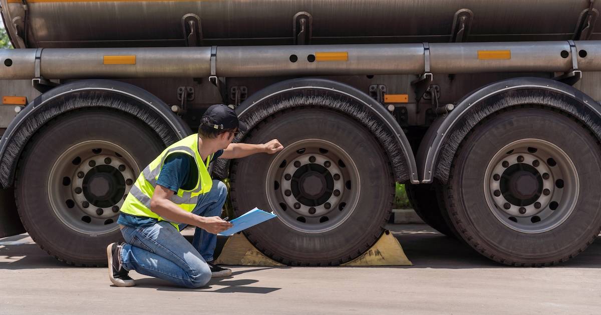 Inspector in a high-visibility vest checking the wheels of a fuel tanker truck
