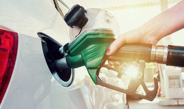 Hand refuelling a white car with a green fuel pump nozzle